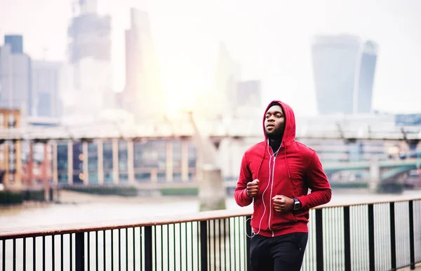 Sportig svart ung löpare kör på bron utanför i en stad. — Stockfoto