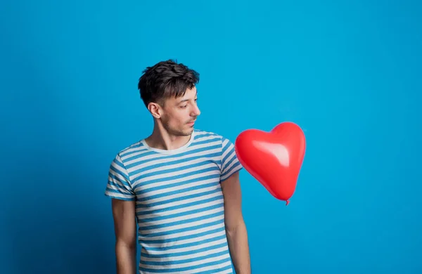 Портрет молодого чоловіка в студії на синьому фоні, дивлячись на червоне серце . — стокове фото