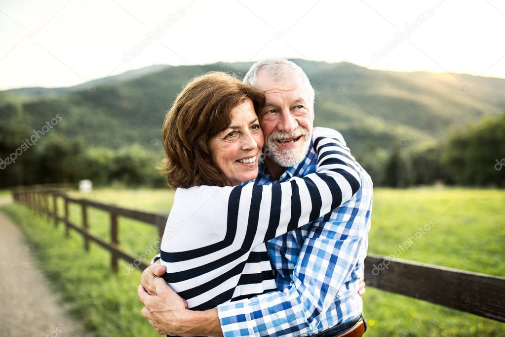 A senior couple hugging outdoors in nature.