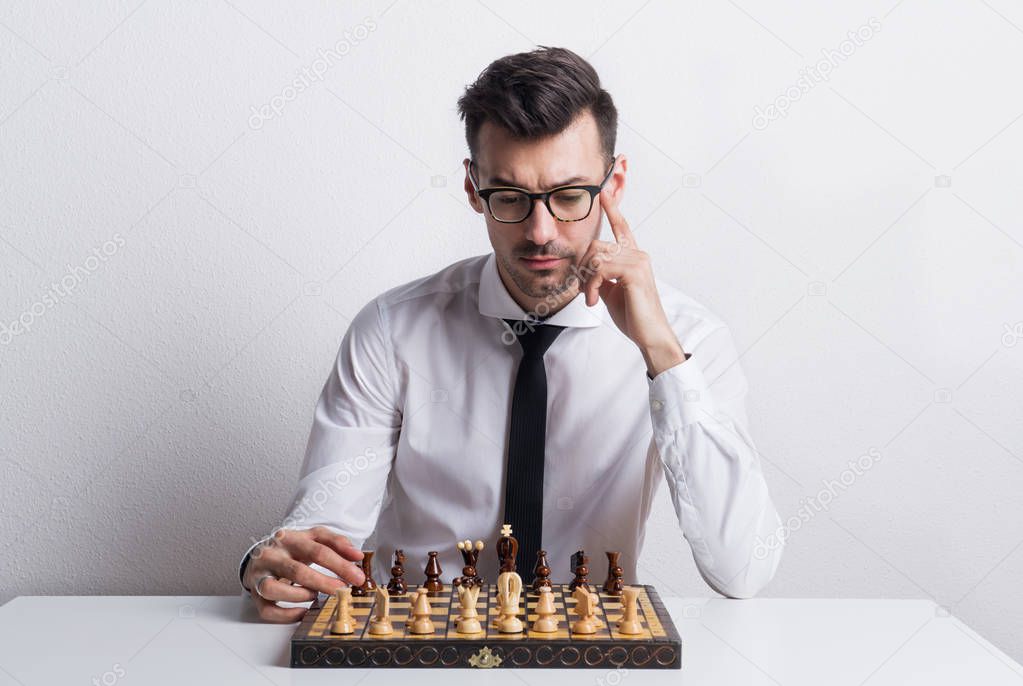 Portrait of a young man in a studio, sitting at the table with chess board game.
