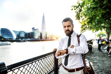 Zaman kontrol hipster işadamı ile Londra, nehir kenarında yürüyüş dizüstü bilgisayar çantası.