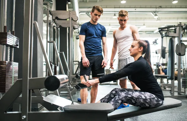 Unga män i gymmet tittar på tränare som tränar på kabel vikt maskin. — Stockfoto