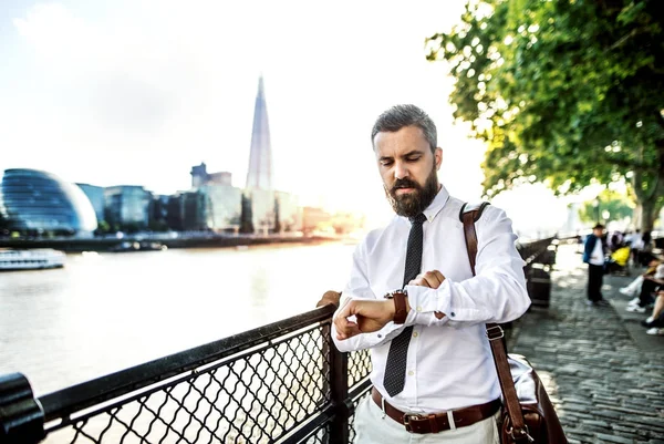 时髦的商人用手提袋在伦敦河边散步, 检查时间. — 图库照片