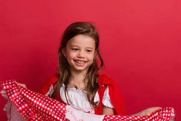 Una bambina in costume Cappuccetto Rosso in studio su sfondo rosso . — Foto Stock