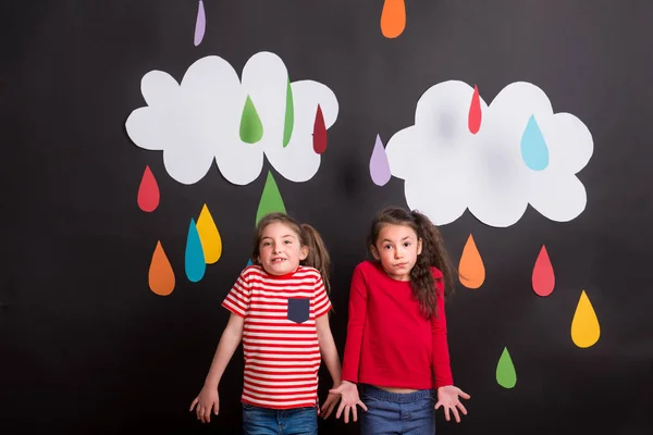 Piccole ragazze in studio, in piedi su sfondo nero con nuvole e gocce di pioggia . — Foto Stock