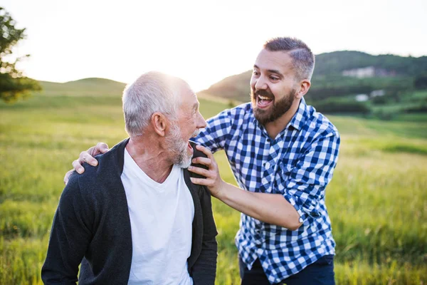 Un figlio hipster adulto con padre anziano in una passeggiata nella natura al tramonto, divertendosi . — Foto Stock