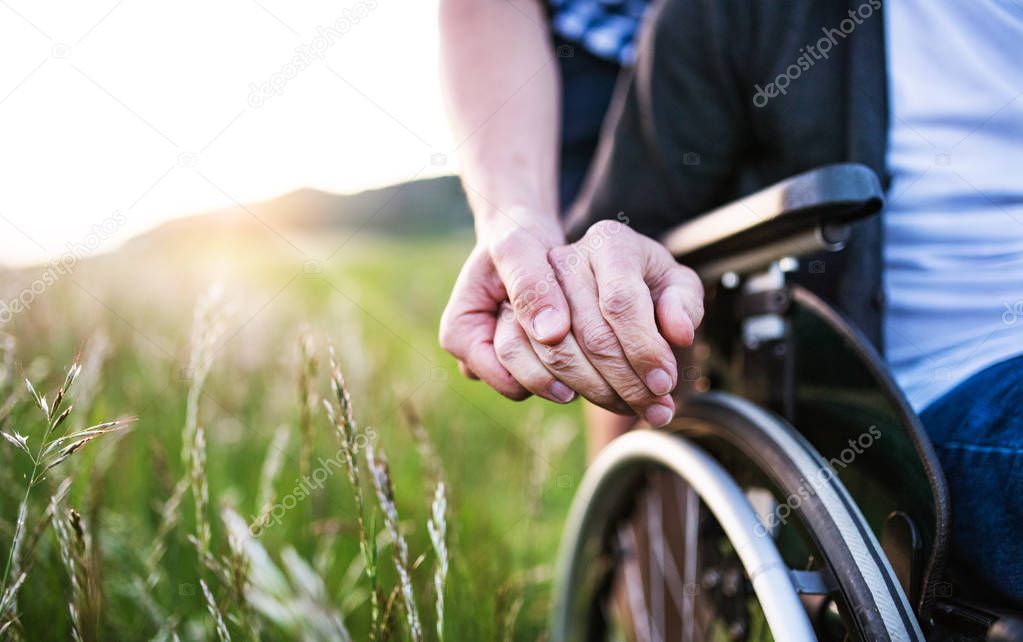 A close-up of unrecognizable son holding his fathers hand on a wheelchair.