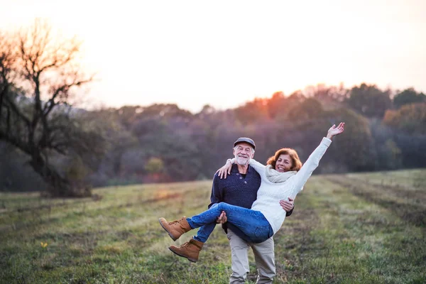 Hombre mayor llevando a una mujer en sus brazos en una naturaleza otoñal al atardecer . —  Fotos de Stock