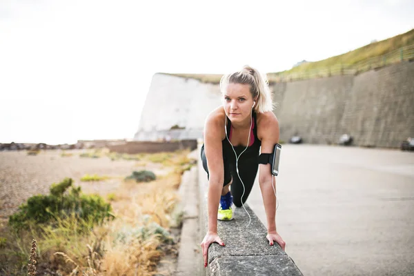 Genç sportif kadın runner kulaklık dışında doğada germe ile. — Stok fotoğraf