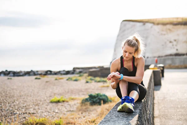 Giovane donna sportiva corridore che riposa fuori nella natura, impostazione smartwatch . — Foto Stock