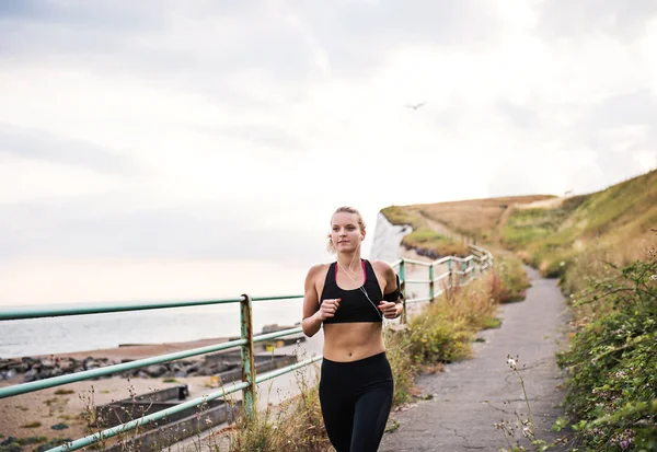 Sportieve jongedame loper met koptelefoon uitgevoerd door de zee in de natuur. — Stockfoto