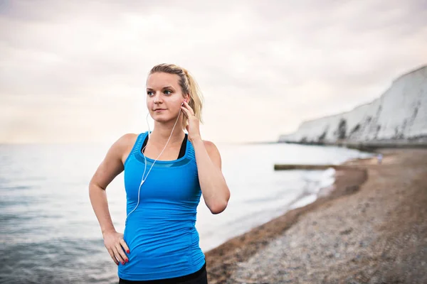 Joven corredora deportiva con auriculares parados en la playa afuera . — Foto de Stock