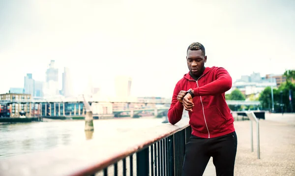 Fiatal sportos fekete férfi futó a hídon kívül a városban, smartwatch beállítása. — Stock Fotó