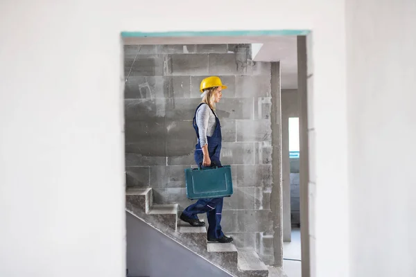 Mulher trabalhadora com uma caixa de ferramentas descendo as escadas no canteiro de obras . — Fotografia de Stock