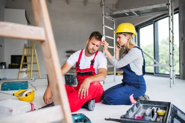 Een vrouw met smartphone helpen man werknemer na een ongeval op de bouwplaats. — Stockfoto