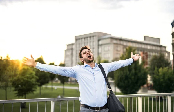 Un homme d'affaires heureux debout sur un pont, hurlant et étirant les bras . — Photo