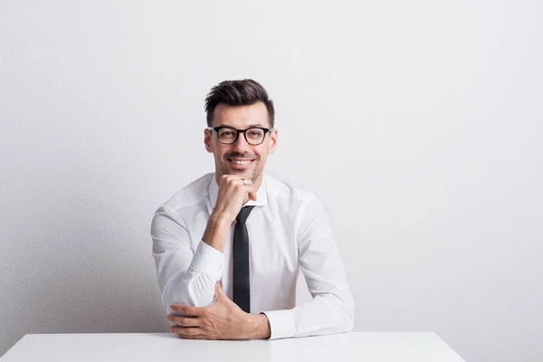 Portret van een jonge man met witte shirt zitten aan de tafel in een studio. — Stockfoto