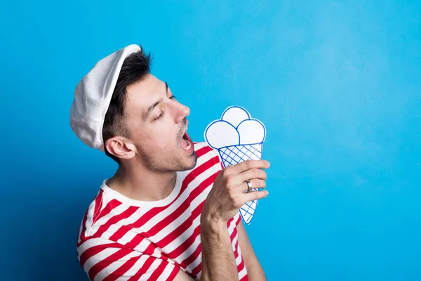 Porträt eines jungen Mannes in einem Atelier mit Schiebermütze, der Eis aus Papier isst. — Stockfoto