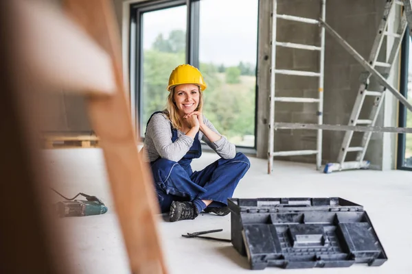 Jonge vrouw werknemer zittend op de vloer op de bouwplaats. — Stockfoto