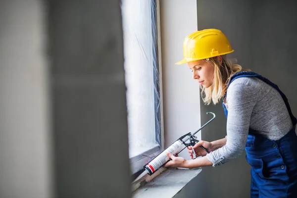 Young woman worker using silicone sealant gun on the construction site. — Stock Photo, Image