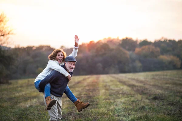 Senior man die geeft een vrouw een piggyback rijden in een herfst natuur. — Stockfoto