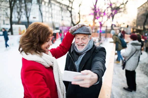 Casal sênior com smartphone em um passeio em uma cidade no inverno . — Fotografia de Stock