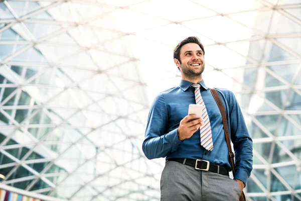 A young businessman with smartphone walking in a modern building, texting. — Stock Photo, Image