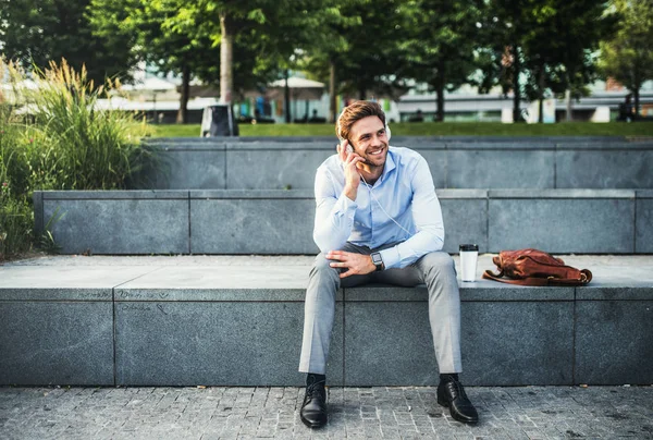 Un uomo d'affari con le cuffie seduto all'aperto sulle scale, ad ascoltare musica . — Foto Stock