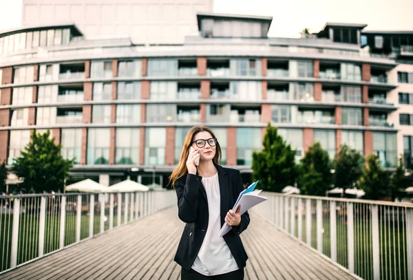 Una joven mujer de negocios con smartphone caminando por el puente en una ciudad . —  Fotos de Stock