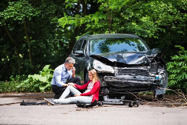 Νεαρή γυναίκα από το αυτοκίνητο μετά από ένα ατύχημα και ένας άνδρας κάνει μια τηλεφωνική κλήση. — Φωτογραφία Αρχείου