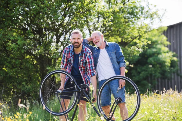 Un hijo hipster adulto y padre mayor reparando pinchazos de bicicleta en un día soleado . —  Fotos de Stock