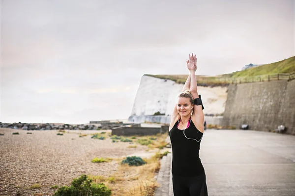 Giovane donna sportiva corridore con auricolari che si estende al di fuori dalla spiaggia . — Foto Stock