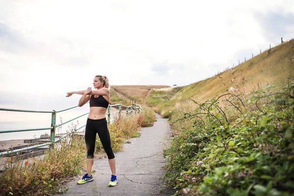 Giovane donna sportiva corridore in activewear nero in piedi fuori nella natura, stretching . — Foto Stock