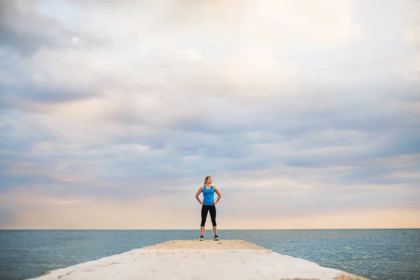 Una giovane donna sportiva in piedi su un molo vicino all'oceano fuori . — Foto Stock