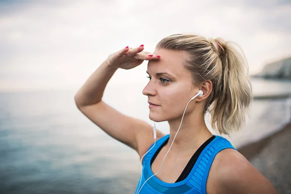Młoda kobieta sportowym biegacz z słuchawki, stojąc na plaży. — Zdjęcie stockowe