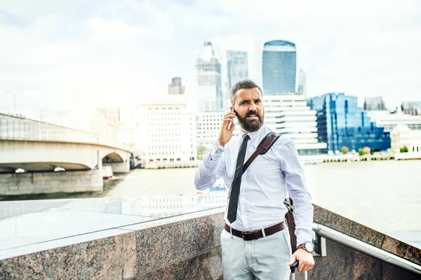 Hipster επιχειρηματίας με smartphone στέκεται δίπλα στο ποτάμι στο Λονδίνο, ζητώντας. — Φωτογραφία Αρχείου