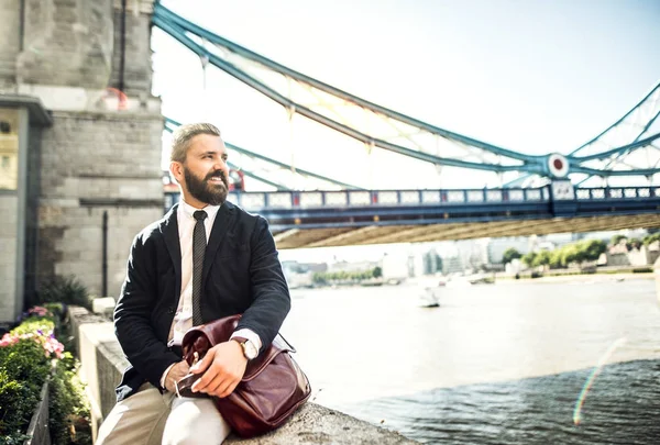 Hipster hombre de negocios con una bolsa sentada junto al Tower Bridge en Londres . — Foto de Stock