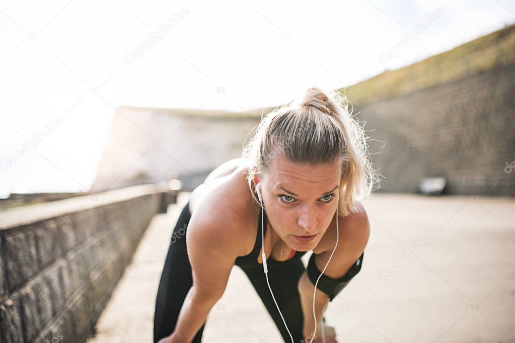 Young sporty woman runner with earphones resting outside by the sea.
