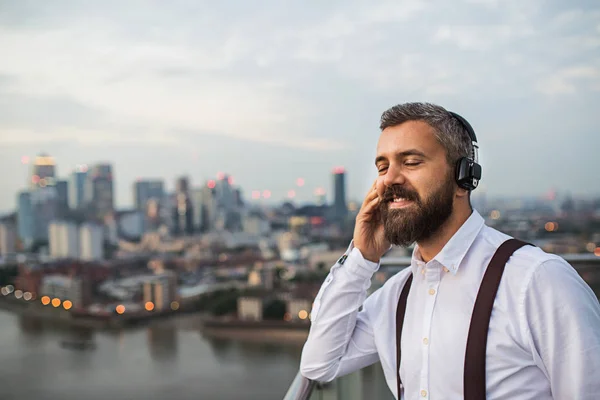 ロンドン パノラマに対して立っているヘッドフォンを持ったビジネスマン. — ストック写真