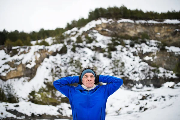 Een portret van de taille-up van senior man die zich uitstrekt voordat de run in de winter natuur. — Stockfoto