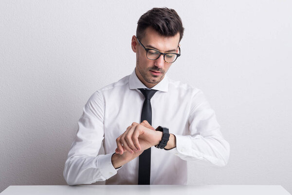 Портрет молодого человека в белой рубашке и умных часах, сидящих за столом
.