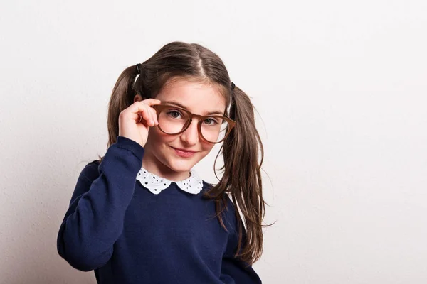 Una piccola scolaretta sfacciata con occhiali e uniforme in uno studio . — Foto Stock