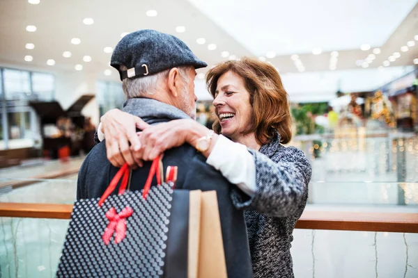 Šťastný starší pár s papírové tašky v nákupním centru, objímání. — Stock fotografie