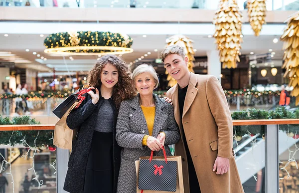 A portrait of grandmother and teenage grandchildren in shopping center at Christmas. — Stock Photo, Image