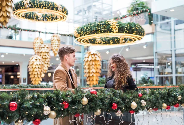 A young couple looking at each other in shopping center at Christmas. — Stock Photo, Image