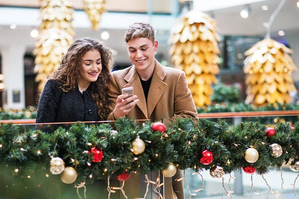 A young couple with smartphone in shopping center at Christmas. — Stock Photo, Image