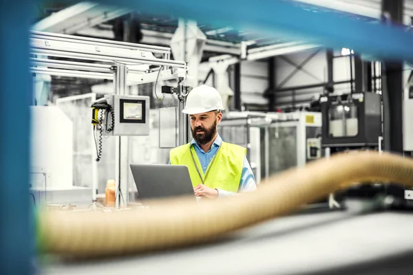 Ett porträtt av ingenjör industriell mannen med laptop i en fabrik, arbetar. — Stockfoto
