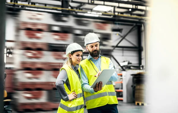 Ένα πορτραίτο ενός βιομηχανικού άντρα και μιας γυναίκας μηχανικού με πλακέτα σε ένα εργοστάσιο, που εργάζονται. — Φωτογραφία Αρχείου