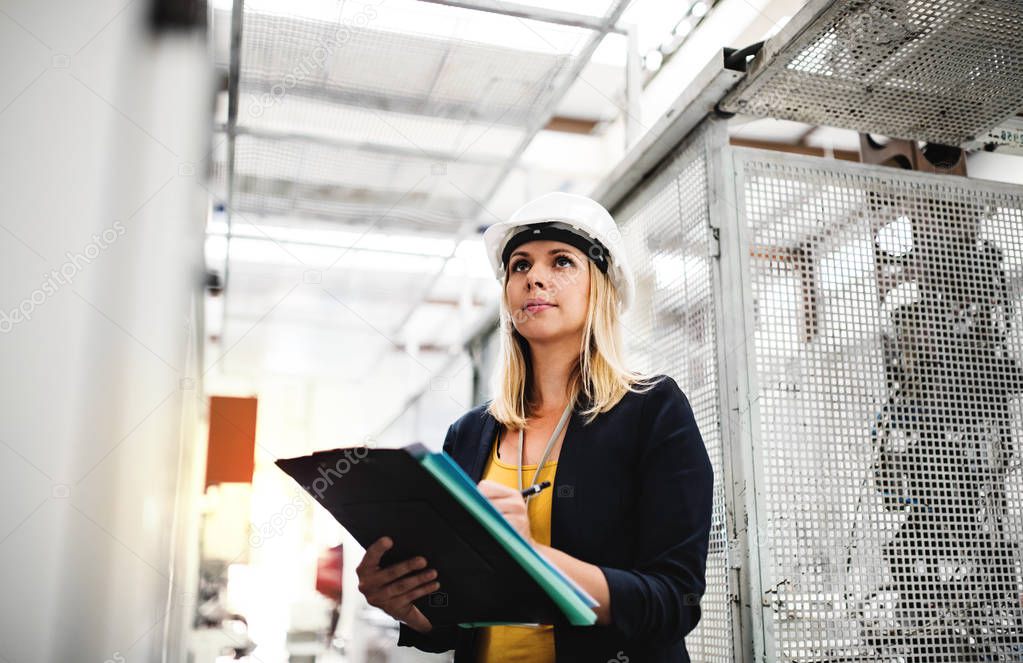 A portrait of an industrial woman engineer in a factory checking something.