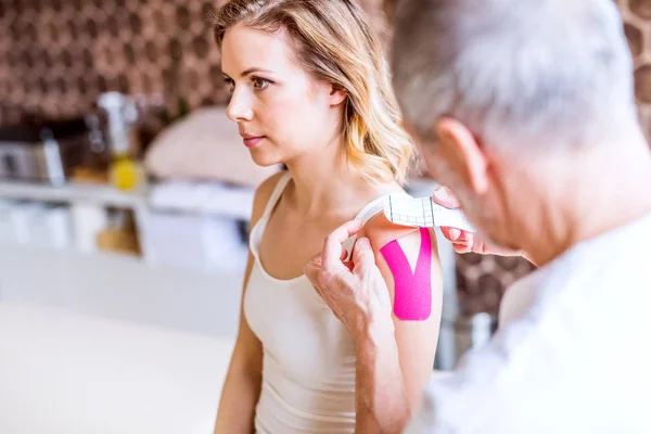 Fisioterapeuta masculino mayor aplicando cinta adhesiva a una paciente femenina. De cerca. . — Foto de Stock